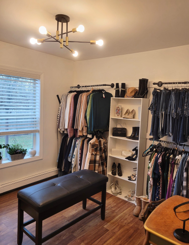 Light-filled master closet featuring a store like clothing rack, shelves with accessories, a dressing bench and makeup desk.