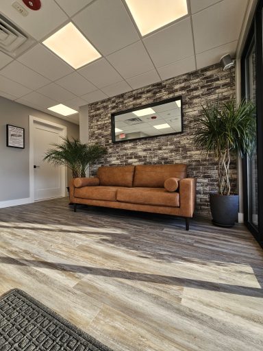 A modern waiting area with a brown couch, stone wall, and indoor plants.