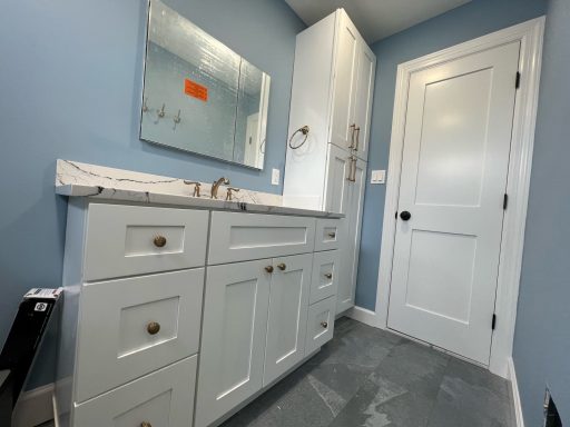 Bathroom featuring a light blue wall, white vanity with drawers, and a door.