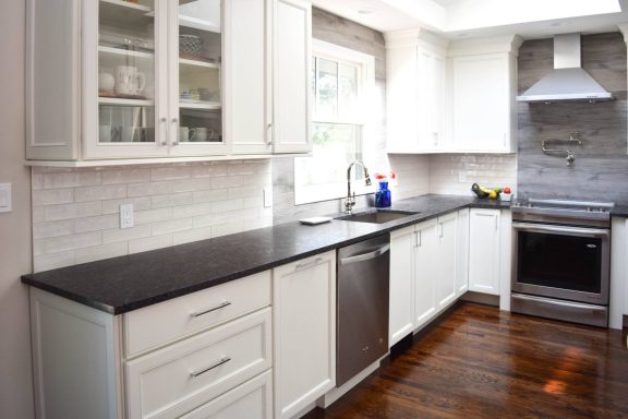 Modern kitchen with white cabinets, black countertops, and stainless steel appliances.