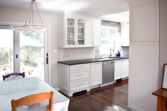 Bright, modern kitchen featuring white cabinets, a dark countertop, and wooden flooring.