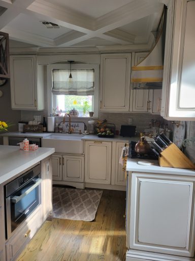 Bright kitchen with white cabinets, a window, and a wooden floor, featuring plants and utensils.