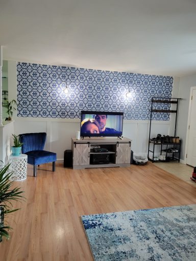 Living room with a blue patterned wall, a TV, a chair, and a decorative rug.