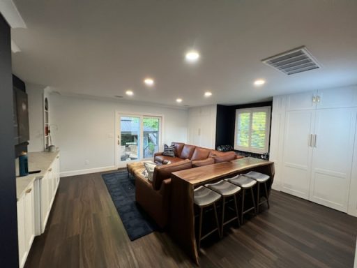 Modern living room with a brown sectional sofa, wooden table, and kitchen area.