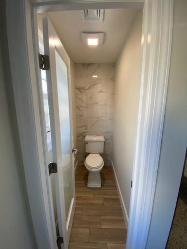 Narrow bathroom with a toilet, light gray walls, and tiled flooring.