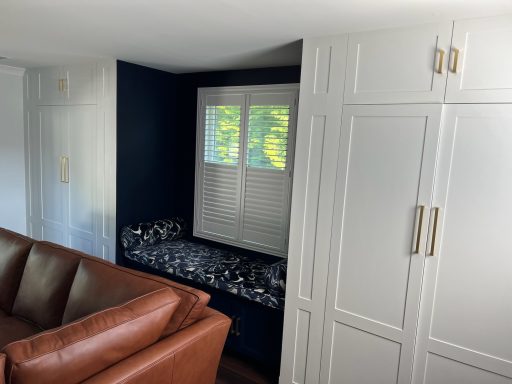 Cozy nook with a dark wall, white shutters, and a brown leather sofa nearby.