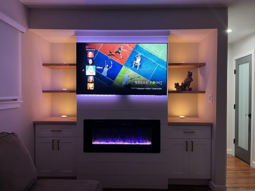 Modern living room with a mounted TV above an electric fireplace and illuminated shelves.