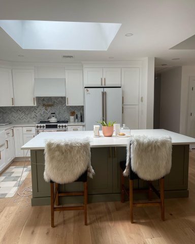 Modern kitchen with a large island, two chairs with fur covers, and natural light from a skylight.