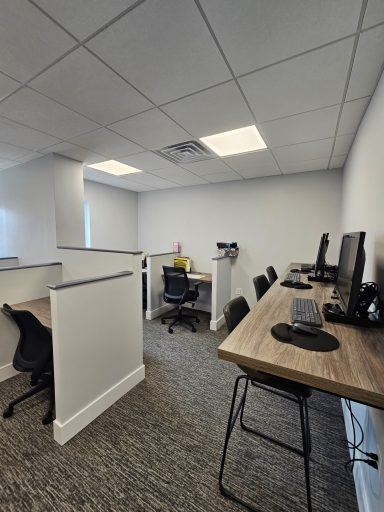 Office space featuring multiple computer desks and ergonomic chairs in a bright, modern setting.