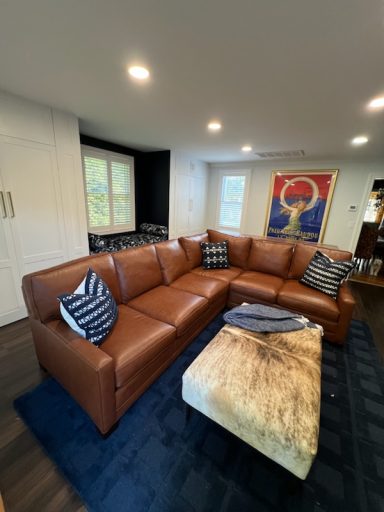 Brown leather sectional couch with striped pillows on a blue rug and a coffee table.