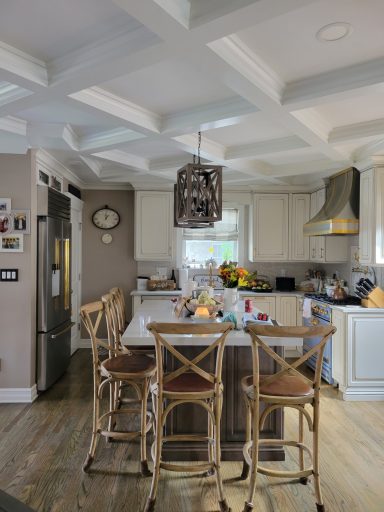 Bright kitchen with white cabinets, a center island, bar stools, and modern appliances and coffered ceiling detail.