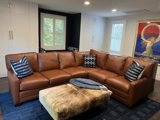 Brown sectional sofa with striped pillows, a fuzzy throw, and a colorful wall poster.