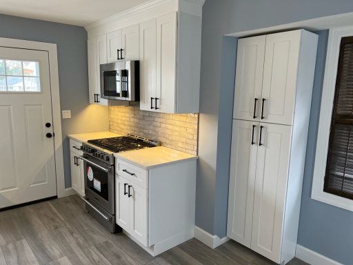 Modern kitchen with white cabinetry, stainless steel appliances, and gray walls.