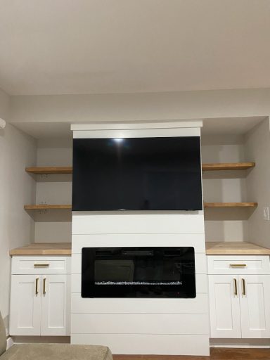 Modern living room with a white entertainment center, shelves, and a mounted TV above a fireplace.