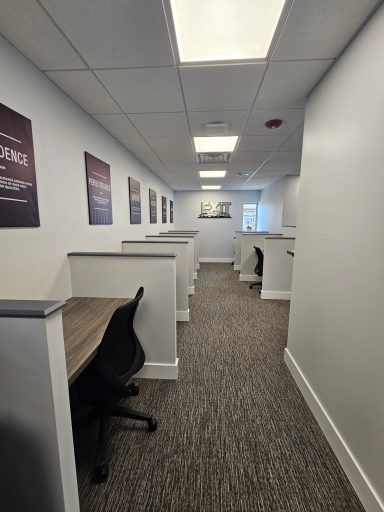 A narrow office corridor with workstations and chairs along both sides.