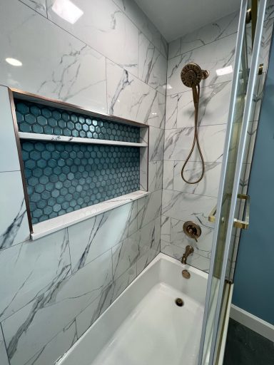 Modern shower with marble walls, blue hexagonal tile niche, and chrome fixtures.