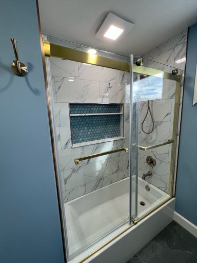 Modern bathroom with a glass shower enclosure, gold accents, and marble walls.