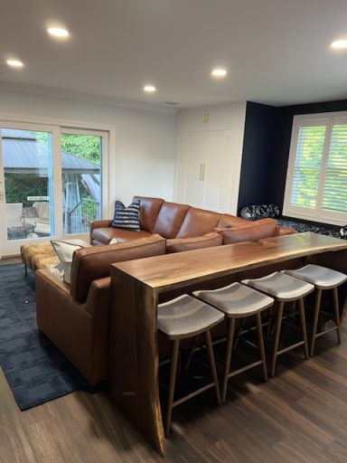 Modern living room with a brown leather sectional and a wooden dining table with bar stools.