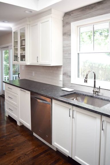 Modern kitchen featuring white cabinets, a stainless steel dishwasher, and a sleek dark countertop.