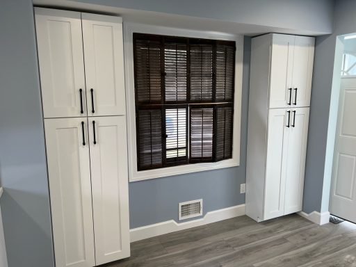 White cabinets flanking a brown window with blinds in a light blue room.