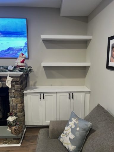 Living room with a gray sofa, white shelves, and a stone fireplace decorated for the holidays.