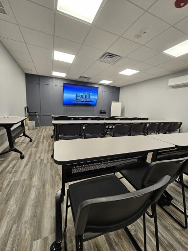 Modern classroom with rows of tables and chairs facing a large screen.